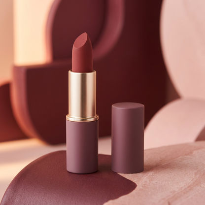 Unbranded rosewood matte lipstick in a dusty mauve and champagne-gold case against a blush and burgundy sculptural background.
